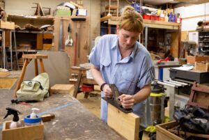 Woman holding a hand-planer working on a piece of wood